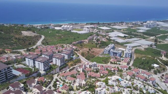 Aerial view of a big hotel complexes, green vegetation and residential buildings on the endless sea background. Clip. Concept of summer holidays and vacation.
