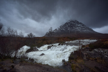 Waterfall to River Etive, Glencoe, Scotland, Uk. River with lots of water, picture in the forest with Stob Dearg mountain in the background. Snowy atmosphere in winter, after a big storm