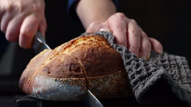 Woman cutting bread at the kitchen. Slicing bread with knife on black wooden cutting board. home cooking process