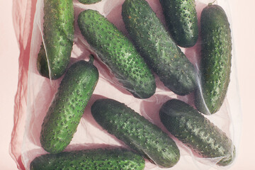 Reusable packaging of products by weight. Cucumbers in a reusable bag close up on a pink background