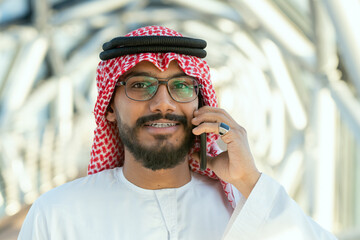 Young Arab delegate or businessman in national attire talking on mobile phone
