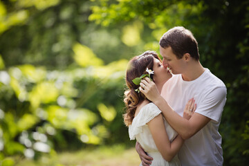 Young man and woman couple in a blooming garden near jasmine bush. Tender holding each other. Spring love story. Brown-haired girl with long hairs with her boyfriend or husband. Young couple on a date
