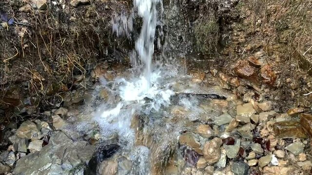 Panning up shot of small waterfall with mudy, mossy pebles. Close-up.