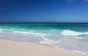 sandy beach with white sea waves, on
turquoise water background