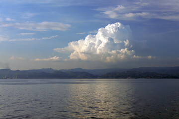 Fototapeta premium White cloud among the clear sky at sunset, over calm sea water
