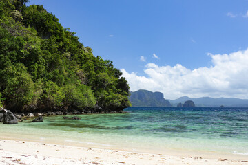 Sandy beach with clear turquoise sea water, mountain covered with vegetation