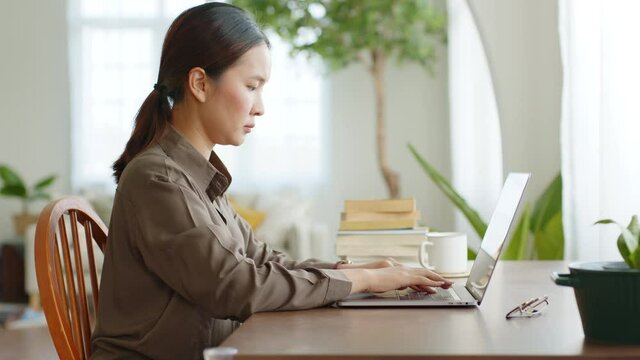 Asian woman working at home, typing on laptop computer seriously