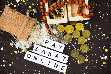 PAY ZAKAT ONLINE word coin stacked, rice grain in bowl and mini house on brown background. Muslim concept for zakat property, income and "fitrah" zakat. Image with selective focus.