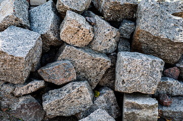 Roughly heaped granite stones, outdoor weathered material, large building blocks. Close-up.
