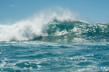A beautiful turquoise breaking wave in the ocean with a clear blue cloudless sky.