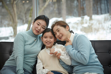 Little kid daughter and old mother while sitting on sofa at home