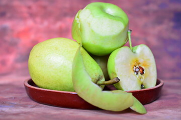 Green fruits, peeled and sliced apples and pear on a brown background