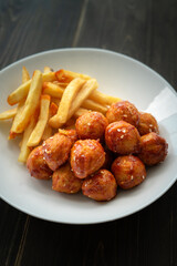 Spicy coated meatballs with spicy sauce served with fried potatoe fries. Korean style snacking.