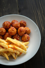Spicy coated meatballs with spicy sauce served with fried potatoe fries. Korean style snacking.
