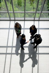 Business partners shaking hands in the modern office. Standing near the window while the sunlight shines on them. There is a shadow on the wooden floor © chadchai