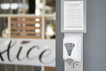 Hand sanitizer machine in public place near the wall at the entrance to shopping center or grocery store. Automatic dispenser with alcohol gel sanitizer
