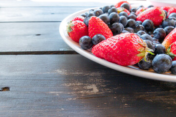 Fresh natural berries of ripe strawberries and blueberries on dark wooden table.
