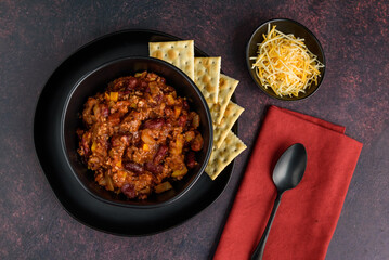 Black bowl of spicy chili con carne on a rustic moody background
