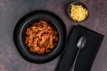 Black bowl of spicy chili con carne on a rustic moody background
