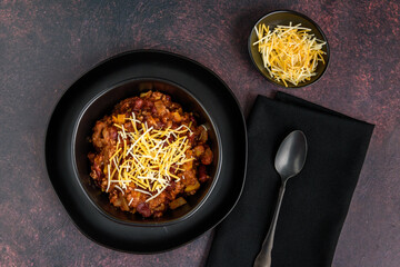 Black bowl of spicy chili con carne on a rustic moody background
