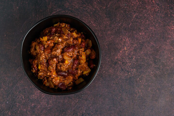 Black bowl of spicy chili con carne on a rustic moody background
