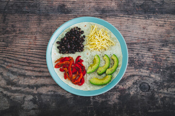 plant-based food, vegan version fo the viral layered tortilla wrap hack with red peppers grated dairy-free cheese avocado and black beans