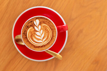 Soft focus Top view close up of hot espresso, latte coffee in a red ceramic cup on blur wood table background.