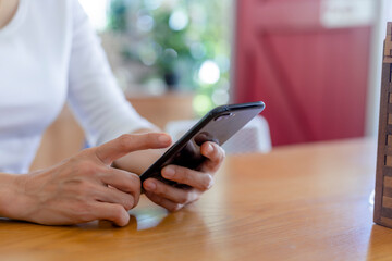 Close up hands of beautiful young woman holding mobile, smart phone sitting in cafe. Soft focus hands of women holding and use cell phone in coffee shop. Tectechnology and lifestyle concept.