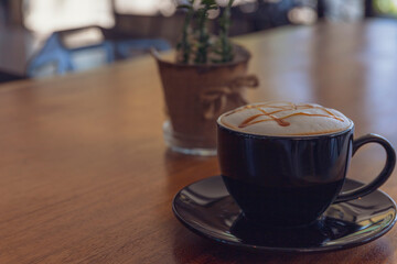 Close up hot cappuccino, latte, caramel macchiato on table with blur coffee shop background. Process with warm vintage tone style.