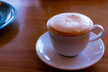 Close up hot cappuccino, latte, caramel macchiato on table with blur coffee shop background. Process with warm vintage tone style.