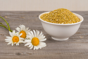 dried chamomile in white bowl and fresh flowers on aged wooden planks