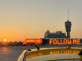 "follow me" light bar on airfield vehicle with sunset control tower background