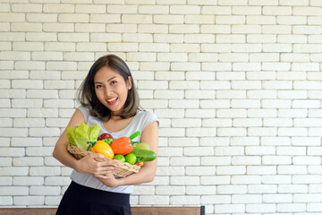 Portrait of smiling beautiful young asian woman holding bucket full of mixed vegetables with copy space. healthy eating concept