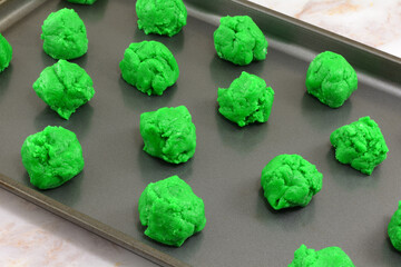 Balls of raw green Saint Patrick's Day cookie batter placed on nonstick baking sheet