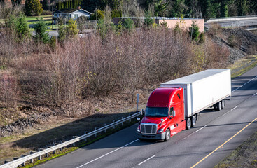 Big rig red semi truck with dry van semi trailer transporting cargo running on the highway road...