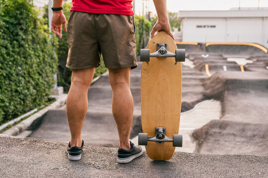 Closeup Asian man holding surfskate or skate board in pumptrack skate Park when sunrise time over photo blur of pumptrack curve, extream sport, healthy and exercise, fashion in covid19 concept