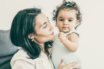 Happy mom holding sweet baby daughter in arms. Cute little girl looking at camera. Copy space. Parenthood and childhood concept