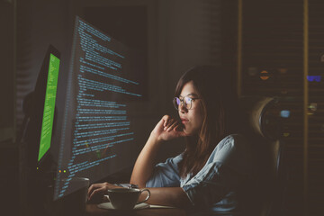 Asian Businesswoman working hard with front of computer desktop with programming source code and...