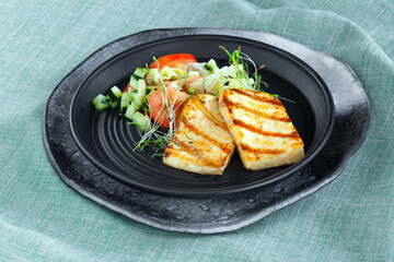 Slices of grilled halloumi cheese with vegetable salad, tomatoes and cucumber
