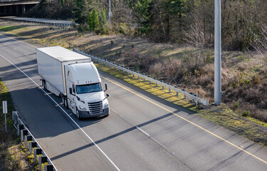 Bonnet white big rig semi truck transporting industrial cargo in dry van semi trailer running on...