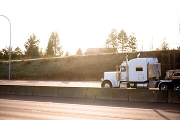 Classic style big rig white semi truck tractor with flat bed semi trailer running on the sunny...