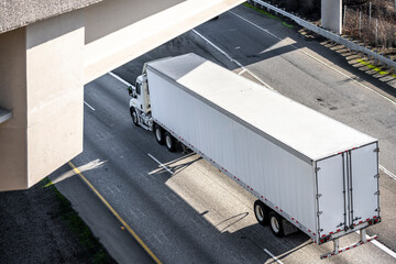 Day cab big rig white semi truck with roof spoiler transporting cargo in dry van semi trailer running on the road under the bridge