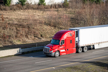 Long haul big rig red semi truck tractor transporting cargo in refrigerator semi truck running on...
