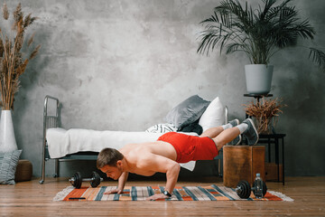 The young man goes in for sports at home. Cheerful sportsman with blond hair does push-ups in the...