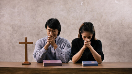 A young Asian Christian couple praying to Jesus Christ in a church.