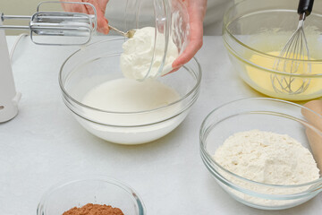 Close up baking process. Chef adds sour cream  into a bowl with whisked egg whites.
