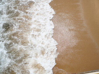 White bubble and green water of sea wave splashing on brown sand of the beach at Aerial view