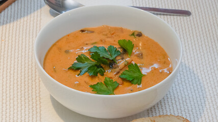 Creamy mushroom soup in a glass bowl served with fresh parsley close up