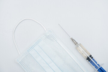 One single syringe with dose of medicine or vaccine with one single protective face mask on white...