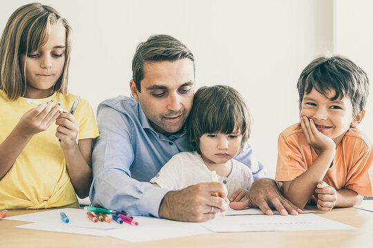 Focused dad and lovely kids drawing with marker on paper. Concentrated Caucasian father painting with pen and playing with children in living room. Fatherhood, childhood and family time concept